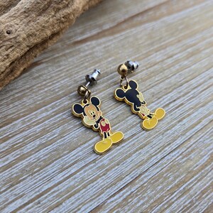 Puede incluir: Un par de pendientes de Mickey Mouse de color dorado. Los pendientes presentan una imagen de dibujos animados de Mickey Mouse con orejas negras, pantalones cortos rojos y zapatos amarillos. Los pendientes est&aacute;n unidos a postes de plata.