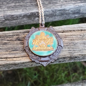 May include: A bronze pendant necklace with a green enamel medallion featuring a gold crest with the text "Forward Together".