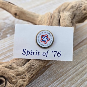 May include: A round pin with the words "American Revolution Bicentennial 1776-1976" encircling a red, white, and blue emblem. The pin is on a white card with the words "Spirit of '76" in blue.