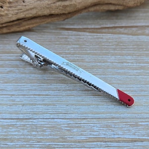 May include: A silver tie clip shaped like a saw blade with a red tip. The tie clip has the text "SIMONDS MADE IN ENGLAND" on it.