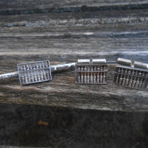 May include: A set of three silver abacus cufflinks and a tie bar. The abacus is a traditional Chinese counting tool.