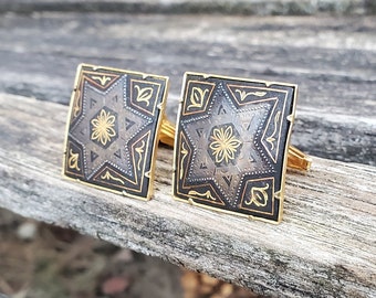 May include: A pair of gold cufflinks with a black enamel background and a silver star design. The star has a gold center with a floral pattern.