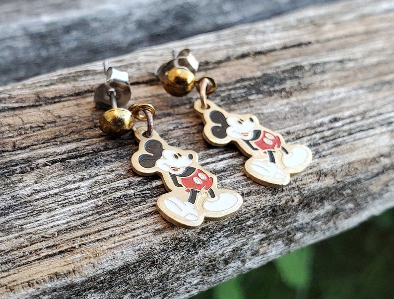 Puede incluir: Un par de pendientes de Mickey Mouse de tono dorado. Los pendientes presentan una imagen de dibujos animados de Mickey Mouse con su caracter&iacute;stico pantal&oacute;n rojo y guantes blancos. Los pendientes est&aacute;n unidos a postes de plata.