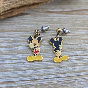Puede incluir: Un par de pendientes de Mickey Mouse de tono dorado. Los pendientes presentan una imagen de dibujos animados de Mickey Mouse con su caracter&iacute;stico pantal&oacute;n rojo y zapatos amarillos. Los pendientes est&aacute;n unidos a postes de tono plateado.