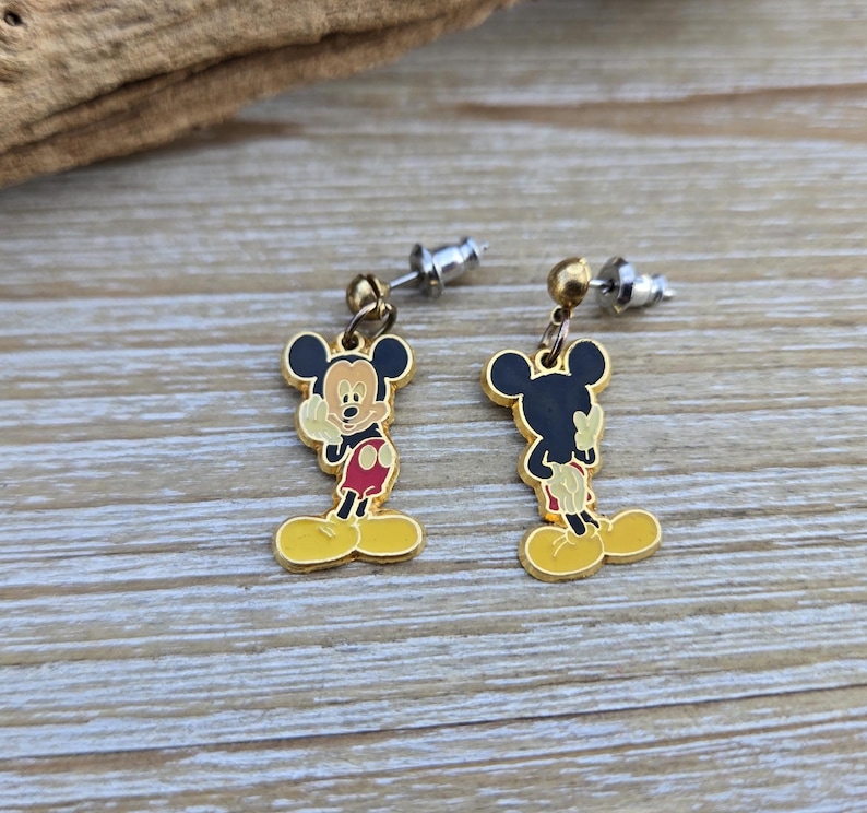 Puede incluir: Un par de pendientes de Mickey Mouse de tono dorado. Los pendientes presentan una imagen de dibujos animados de Mickey Mouse con su caracter&iacute;stico pantal&oacute;n rojo y zapatos amarillos. Los pendientes est&aacute;n unidos a postes de tono plateado.