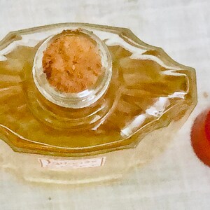Pu&ograve; includere: Una bottiglia di vetro trasparente con un tappo di sughero e un tappo di plastica rosso. La bottiglia &egrave; piena di un liquido giallo chiaro.