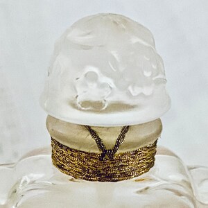 May include: A white glass bottle stopper with a decorative design and a gold band around the top.