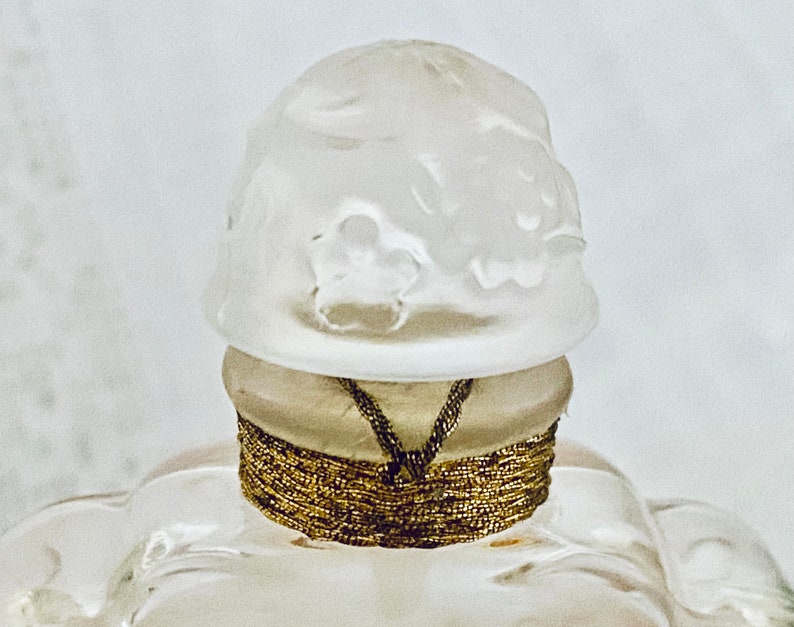 May include: A white glass bottle stopper with a decorative design and a gold band around the top.