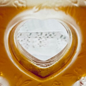 May include: A close-up of a heart-shaped opening in a glass bottle, revealing a white background with a lace pattern.