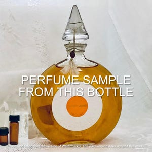 May include: A round, clear glass perfume bottle with a decorative, pointed stopper. The bottle is filled with a golden liquid and has a white label with an orange circle. The text "PERFUME SAMPLE FROM THIS BOTTLE" is overlaid on the image. Several small brown sample bottles are also visible.