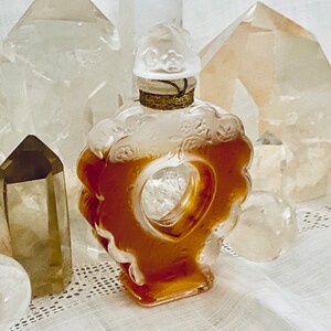 May include: A heart-shaped glass bottle with a gold stopper and a floral design. The bottle is filled with a golden liquid and is surrounded by clear quartz crystals.