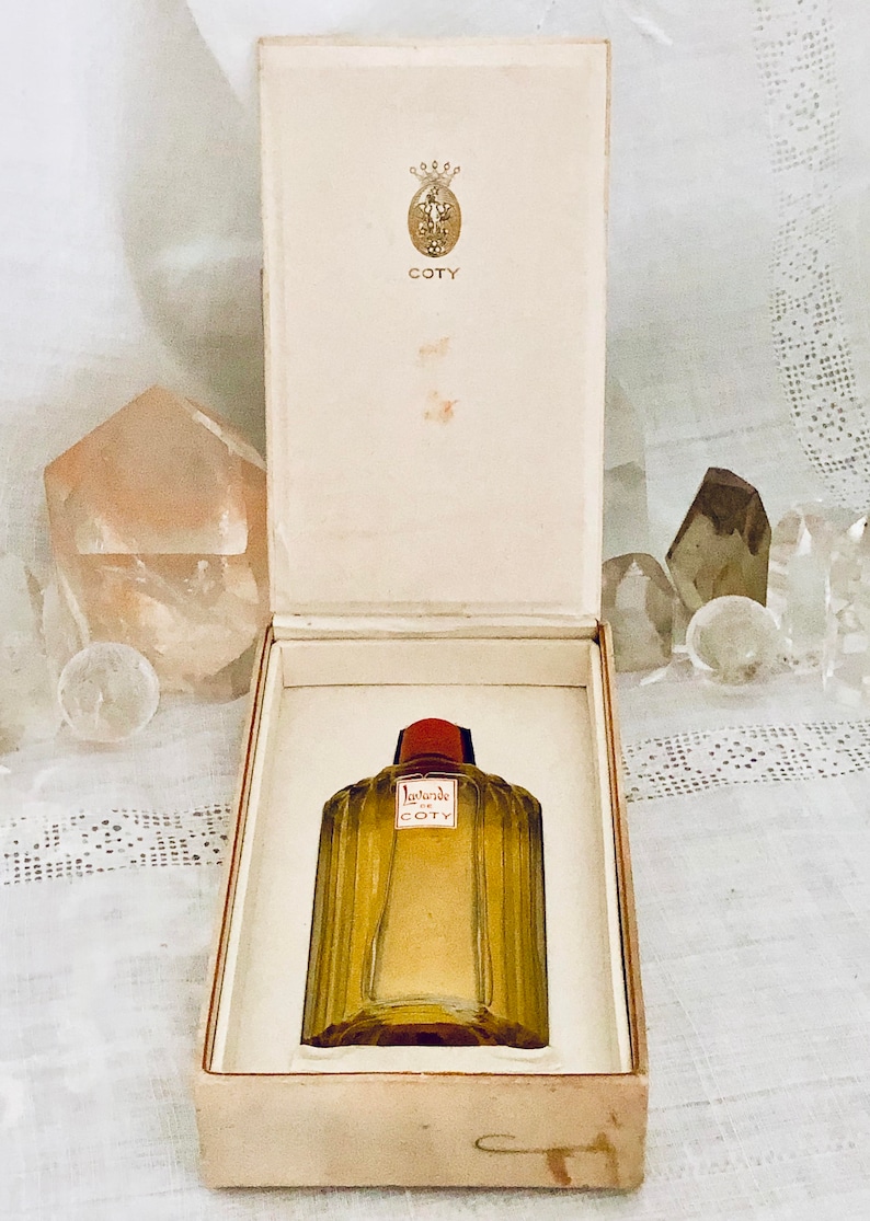 Pu&ograve; includere: Un flacone vintage di profumo Coty L'Aimant in una scatola bianca. Il flacone &egrave; in vetro trasparente con un tappo rosso e lettere dorate. La scatola ha una corona dorata e la parola "Coty" stampata su di essa.