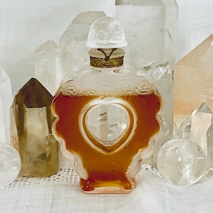 May include: A heart-shaped glass bottle with a gold lid and clear liquid inside. The bottle is surrounded by clear and brown crystals.