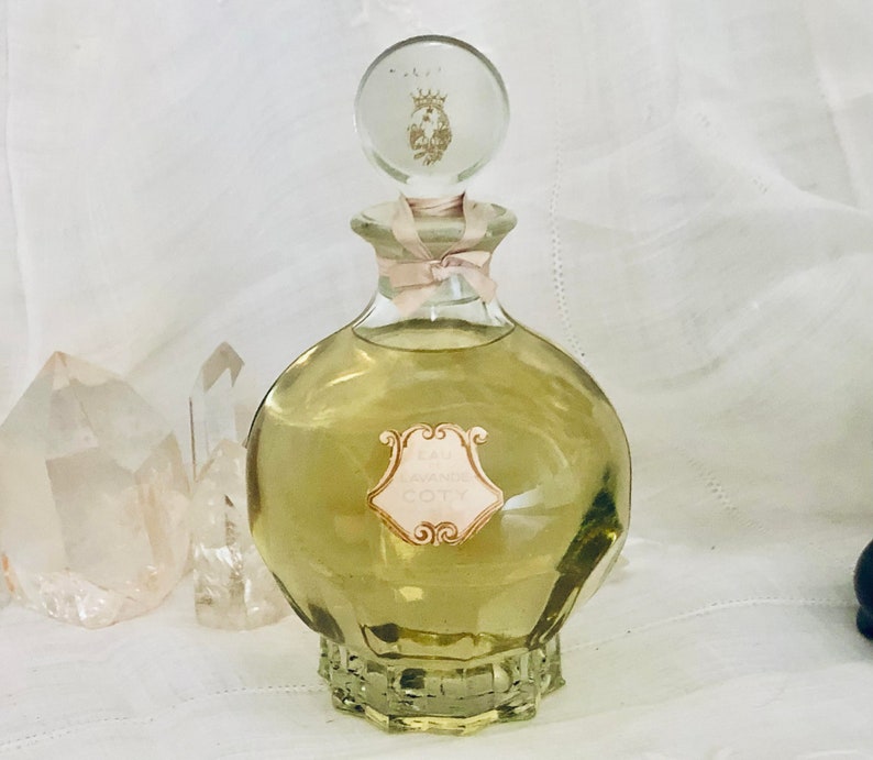 K&ouml;nnte beinhalten: Eine Vintage-Glasflasche mit Eau Sauvage von Coty Parfum. Die Flasche ist klar und hat eine strukturierte Oberfl&auml;che. Das Etikett ist goldfarben und rosa mit dem Text "Eau Sauvage Coty".