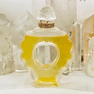 May include: A clear glass perfume bottle with a heart-shaped design and a gold cap. The bottle is filled with a yellow liquid and is surrounded by clear quartz crystals.
