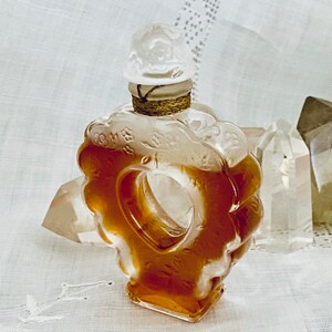 May include: A clear glass bottle with a heart-shaped design and a white stopper. The bottle is filled with a golden liquid and is surrounded by clear crystals.
