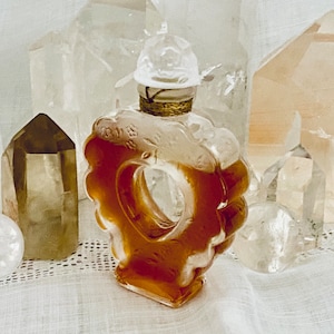 May include: A heart-shaped glass bottle with a gold stopper and a clear liquid inside. The bottle is surrounded by clear and brown crystals.
