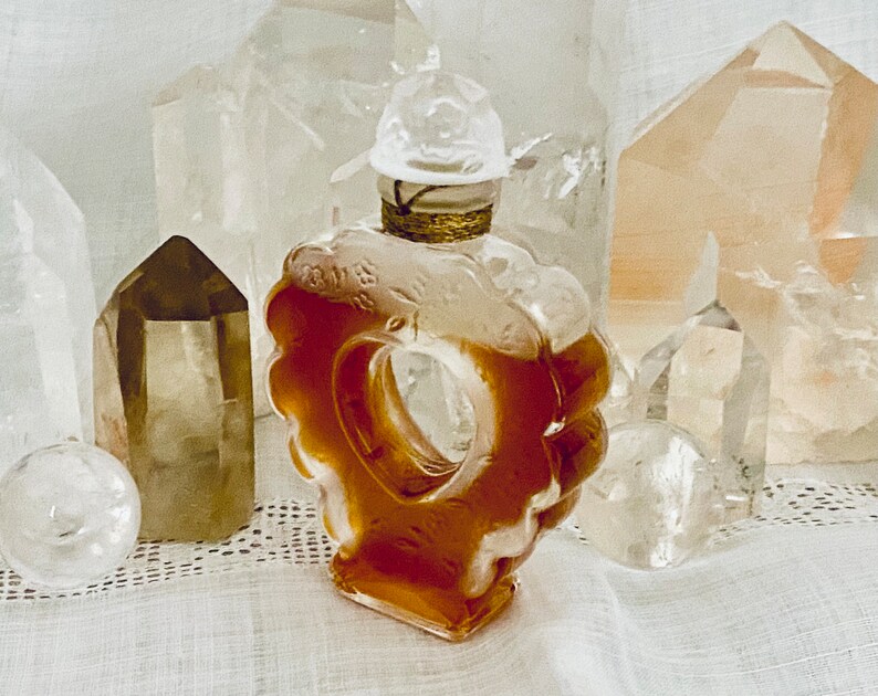 May include: A heart-shaped glass bottle with a gold stopper and a clear liquid inside. The bottle is surrounded by clear and brown crystals.