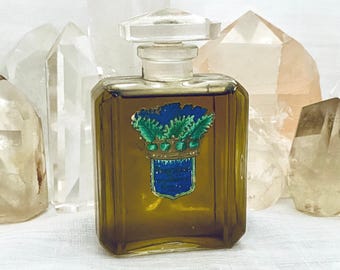 May include: A vintage perfume bottle with a clear, geometric stopper. The bottle contains a golden liquid and has a blue and green crest design. Several clear quartz crystals are in the background.