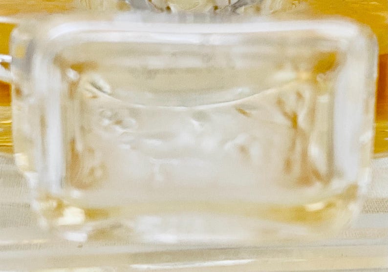 May include: A clear glass bottle stopper with a decorative design of a floral motif. The stopper is designed to fit a bottle of wine or liquor.