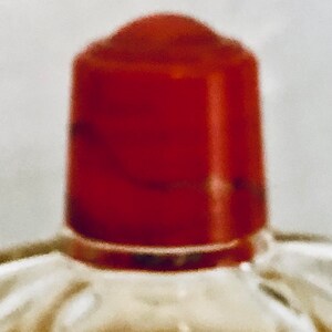Pu&ograve; includere: Un tappo per bottiglia rosso in vetro con una superficie testurizzata. Il tappo &egrave; trasparente e lucido.