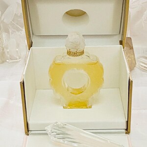 May include: A clear glass bottle of perfume with a gold cap and a heart-shaped design. The bottle is in a pink and gold box with the words "Coeur Joie Nina Ricci" on the bottom.