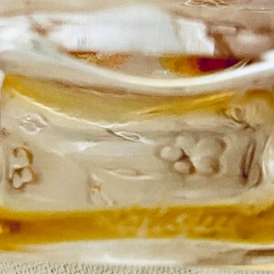 May include: Close-up of a clear glass bottle with a floral design etched into the glass. The bottle is filled with a golden liquid.