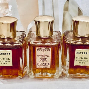 May include: Three vintage glass perfume bottles with gold caps and labels. The bottles contain amber-colored liquid. The labels read "Sabrina Funél Le Cannet Paris", "Bouquet 6 Funél Parfumeur Riviera", and "Esterel Funél Le Cannet Paris".