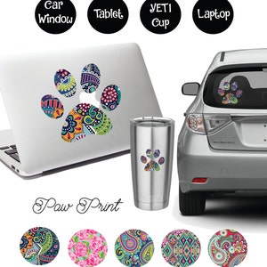 Op de afbeelding: Een kleurrijke paisley-pootafdruk sticker. De sticker is te zien op een laptop, een Yeti-beker en een autoruit. De sticker is ook verkrijgbaar in vijf verschillende kleuren.