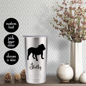 May include: A stainless steel tumbler with a black silhouette of a bulldog and the name "Shelby" printed on it. The tumbler has the Yeti logo on the bottom.
