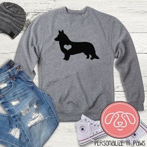 Może przedstawiać: Szara bluza z czarnym siluetem Cardigan Welsh Corgi z białym sercem na klatce piersiowej. Tekst "PERSONALIZE IT PAWS" znajduje się na dole obrazu.