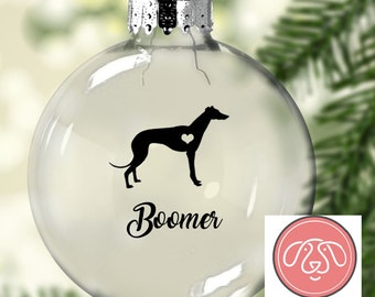 May include: Clear glass Christmas ornament with a black silhouette of a Greyhound dog with a heart on its chest. The ornament is personalized with the name "Boomer".