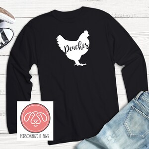 May include: Black long-sleeve shirt with a white silhouette of a chicken and the text "Peaches".