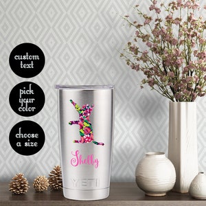 May include: A stainless steel tumbler with a pink floral cat design and the name "Shelby" in pink lettering. The tumbler has a black lid and a silver Yeti logo.