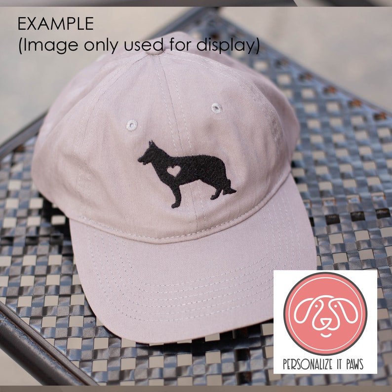 May include: A gray baseball cap with a black embroidered silhouette of a German Shepherd with a heart on its chest. The cap has a curved brim and a white logo that says "PERSONALIZE IT PAWS".