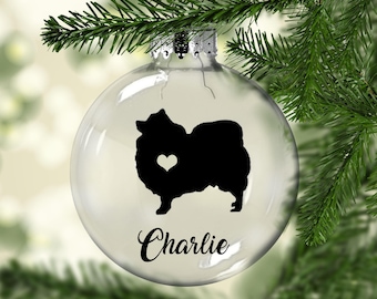 Könnte beinhalten: Klarer Weihnachtsbaumschmuck aus Glas mit einer schwarzen Silhouette eines Zwergspitz mit einem weißen Herzen auf der Brust. Der Schmuck ist mit dem Namen "Charlie" personalisiert.