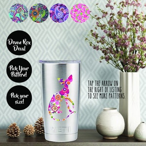 Könnte beinhalten: Ein Yeti-Becher aus Edelstahl mit einem Aufkleber eines Devon Rex-Katers in einem Blumenmuster. Der Aufkleber ist in verschiedenen Mustern erhältlich, darunter Paisley, Blumen und geometrische Muster. Der Becher steht auf einem Tisch mit einer Blumenvase und anderen Dekorationsartikeln.