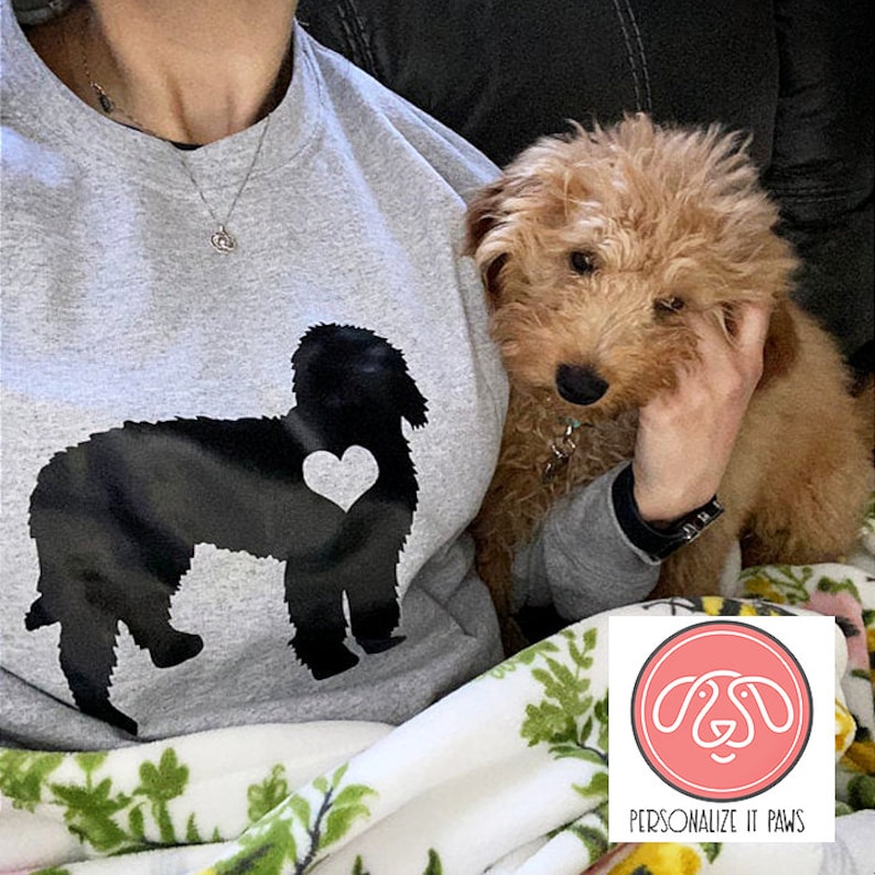 May include: A gray sweatshirt with a black silhouette of a dog with a heart on its chest. The sweatshirt is being worn by a person holding a small brown dog. The text "PERSONALIZE IT PAWS" is on a pink circle with a white outline.