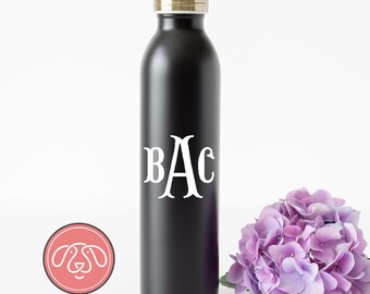 Puede incluir: Una botella de agua negra de acero inoxidable con una tapa dorada y letras blancas con monograma "BAC". Una flor de hortensia morada está al lado de la botella. El logotipo "Personalize it Paws" está en la esquina inferior izquierda.