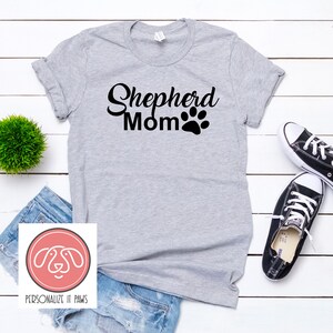 May include: Gray t-shirt with the text "Shepherd Mom" and a black paw print.