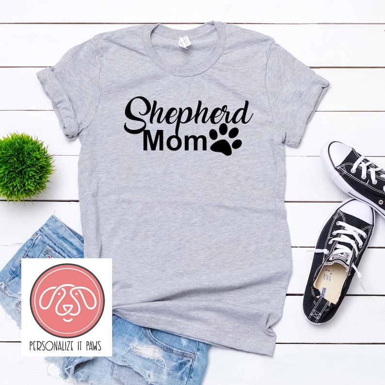 May include: Gray t-shirt with the text "Shepherd Mom" and a black paw print.