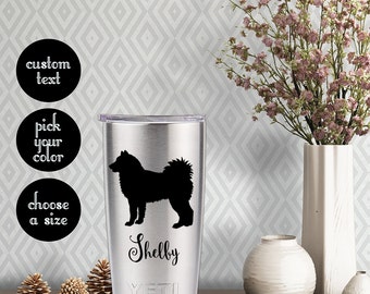 May include: Stainless steel tumbler with a black silhouette of a dog and the name "Shelby" on it. The tumbler is on a wooden surface with pine cones and a white vase.