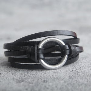 May include: A black leather bracelet with a silver ring accent. The bracelet is made of multiple layers of leather and is adjustable.