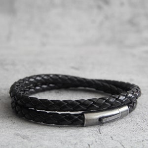 May include: A black leather bracelet with a braided design and a silver metal clasp.