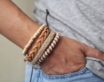 May include: A collection of bracelets in various styles. One bracelet features light-colored wooden beads, another has a braided leather design, and a third is made of woven jute. The fourth bracelet has a white and brown rope design.