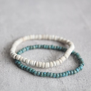 May include: Two beaded bracelets, one white and one blue, stacked on top of each other.