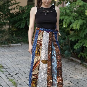 Peut inclure: Un haut noir sans manches avec une encolure en dentelle et une jupe portefeuille composée d'un patchwork de motifs géométriques et floraux variés dans des tons de bleu, marron, blanc et jaune, assorti de sandales compensées à brides marron.