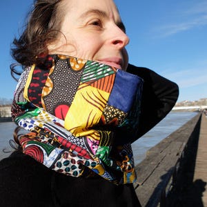 Peut inclure: Un tour de cou coloré fait de chutes de tissu dans un design patchwork. Le tissu est un mélange de couleurs vives, dont le rouge, le jaune, le bleu, le vert et le noir. Le tour de cou est porté par une personne aux cheveux bruns.