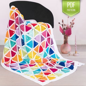 May include: A colorful crochet blanket with a geometric pattern of triangles in shades of red, orange, yellow, green, blue, purple, and white. The blanket is draped over a black chair.