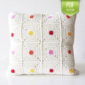 May include: White crochet pillow cover with a geometric pattern and colorful star accents. The pillow cover is made with a white yarn and features a repeating square pattern with a star in the center of each square. The stars are in various colors, including red, pink, yellow, and orange.
